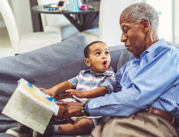 Photo of African American grandchild and grandfather read a book together at home