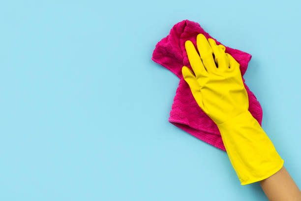 istock Woman's hand in yellow rubber glove wipe by rag blue background. 1265066164