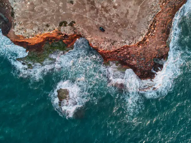 Aerial photo view from above rocky mountain coastline and Mediterranean Sea waters surf sunrise light. Breaking waves raging ocean background. Costa Blanca, Torrevieja shore. Spain
