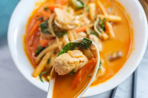 Thai food spicy coconut milk panang curry soup with chicken snow peas onions and spinach