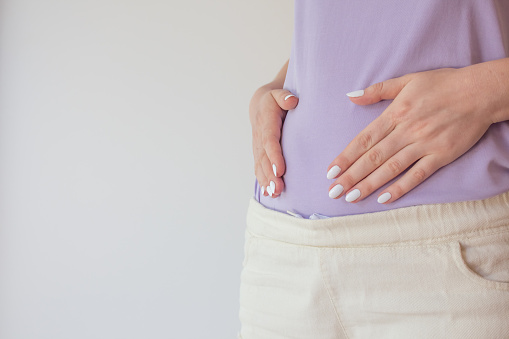 Pregnant woman in the early stages touches the belly with her hands. First and second trimester of pregnancy.