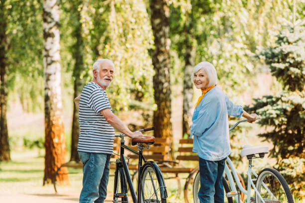 istock Senior couple smiling at camera while standing near bicycles in park 1265072205