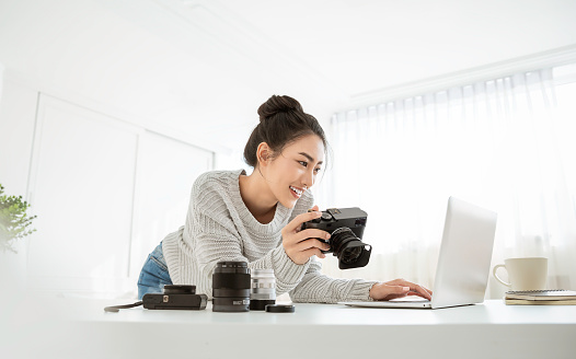 Portrait of beautiful asian photographer woman working in office desk holding camera with laptop. Business people employee freelance online marketing.  Successful freelance creative artist girl business concept