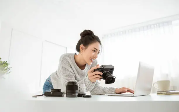 Photo of Portrait of beautiful asian photographer woman working in office desk holding camera with laptop. Business people employee freelance online marketing.  Successful freelance creative artist girl business concept