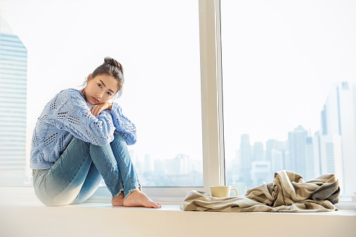 Portrait of beautiful asian woman feeling depress stress in bedroom. Sad face asian girl sit near city view window in winter. Beauty perfect clear skin japanese korean makeup  lifestyle banner