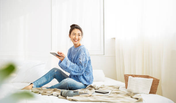 Asian woman with smile use tablet smartphone in blue winter sweater work home, Portrait young beauty asia girl relax in bedroom. Technology people connection digital online market banner Asian woman with smile use tablet smartphone in blue winter sweater work home, Portrait young beauty asia girl relax in bedroom. Technology people connection digital online market banner kids winter fashion stock pictures, royalty-free photos & images