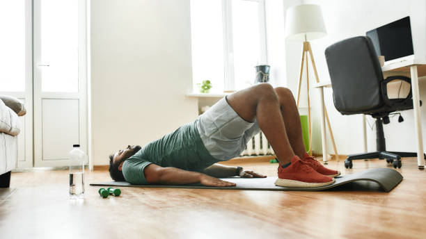 istock Exercising. Young active man doing exercises during morning workout with dumbbells on yoga mat at home. Sport, healthy lifestyle 1265080058