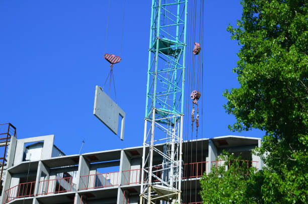 Construction of a multi-storey residential building. Construction crane with a concrete slab. Happy against the blue sky.