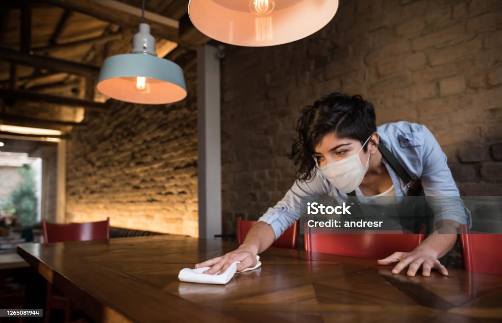 Waitress at a restaurant wearing a facemask and cleaning the tables Waitress at a restaurant wearing a facemask and cleaning the tables during the COVID-19 pandemic - reopening of businesses concepts Restaurant Stock Photo