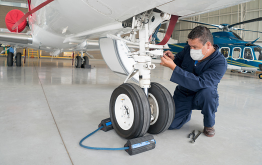 Engineer working at the airport wearing a facemask while fixing an airplane's landing gear