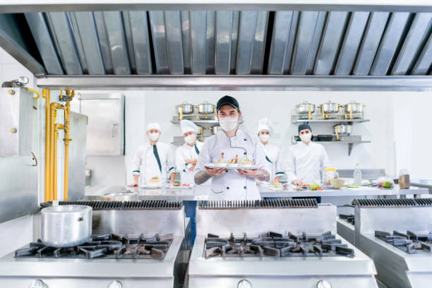 istock Cook wearing facemask in a commercial kitchen while presenting a plate 1265081972