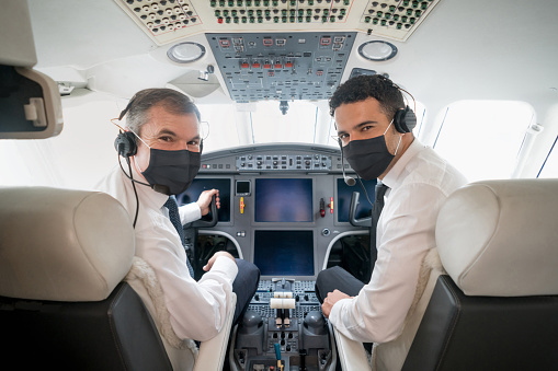 Portrait of two handsome pilots ready to fly an airplane and wearing a facemask while looking at the camera during the COVID-19 pandemic