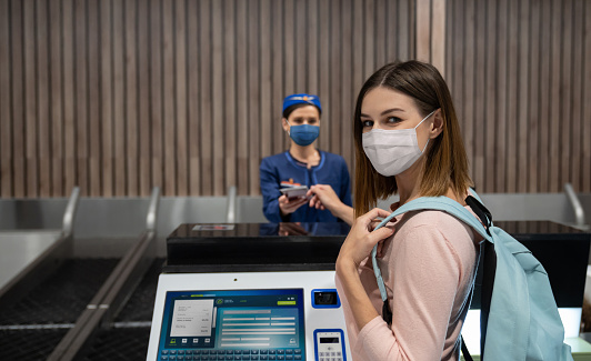 Portrait of a traveling woman doing the check-in at the airport wearing a facemask during the COVID-19 pandemic - travel concepts