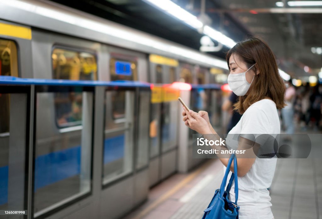 Asian woman texting at the metro station wearing a facemask Asian woman texting at the metro station on her cell phone wearing a facemask to avoid an infectious disease Taiwan Stock Photo