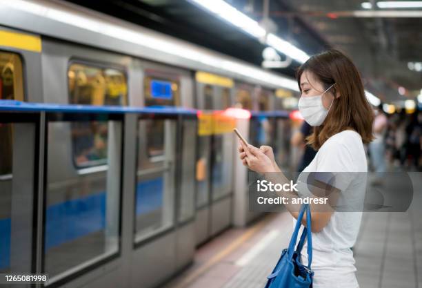 Asian Woman Texting At The Metro Station Wearing A Facemask Stock Photo - Download Image Now