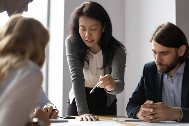 Confident Asian businesswoman talk with diverse colleagues at meeting Confident Asian female team leader talk explain business idea to diverse colleagues at meeting, motivated young ethnic businesswoman speak negotiate brainstorm with multiracial coworkers at briefing graphite stock pictures, royalty-free photos & images