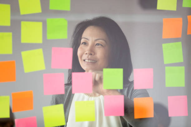 istock Smiling Asian female employee write ideas on sticky notes 1265084585