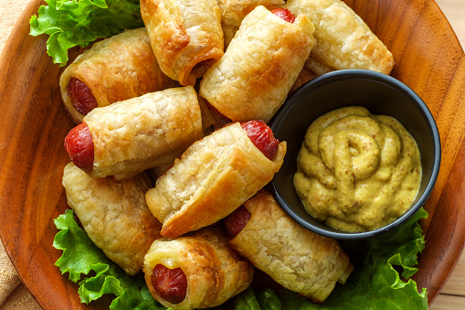 Crispy pigs in a blanket cocktail hotdogs wrapped in croissant dough served with spicy mustard