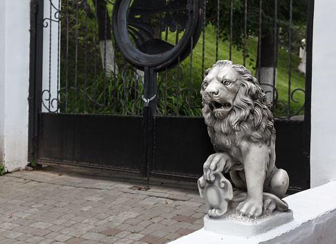 Decorative white stone lion statue near forged gates of a garden