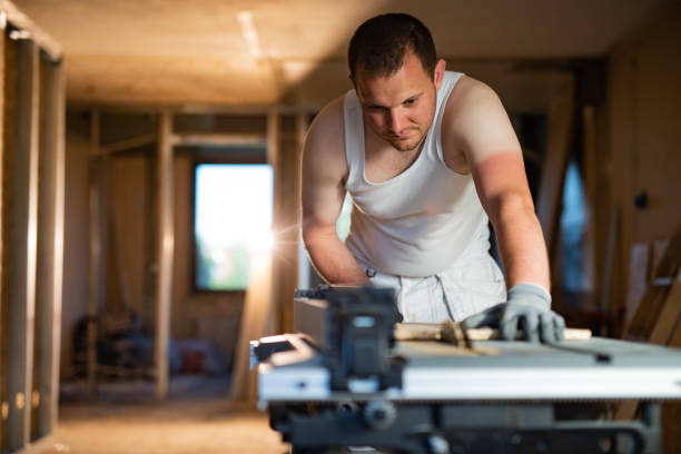 Construction worker cutting plank with circular saw at construction site.