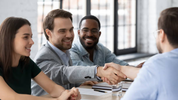 istock Smiling business people shaking hands, sitting at table in boardroom 1265093313