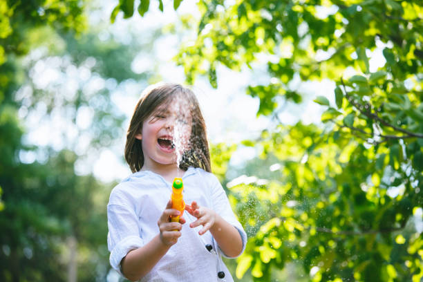 Happy cute boy screaming while shooting and splashing water with squirt gun. Backyard water fun during the summer of COVID-19.