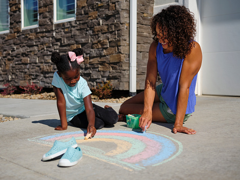 Little child drawing rainbow with colorful chalk on asphalt, closeup