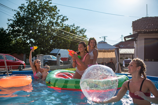 Pool party with friends and family. Summer time. Beautiful women enjoying summer holiday with their children. They are playing with water ball.