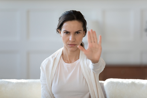 Serious confident young girl looking at camera, showing hand with stop gesture, demonstrating sign against domestic violence against women, condemning discrimination or protesting against abortion.