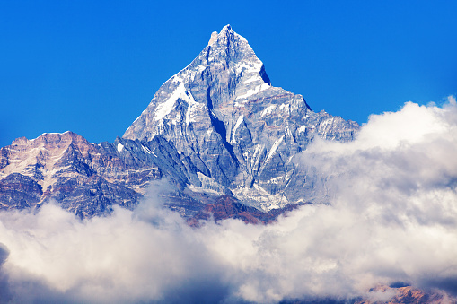 Bright sun in the deep blue high altitude skies above the clouds swirling through the snow capped peaks of the Himalayan mountains, from Ama Dablam to Makalu and Lhotse, Nepal.