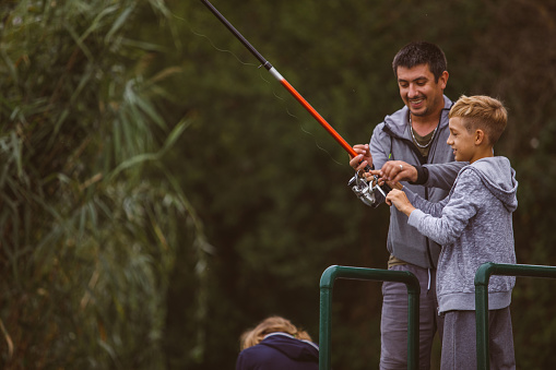 A father teaches his son how to use a fly fishing rod.  The boy smiles with excitement and joy at the camera. Shot in the beautiful Pacific Northwest at Trillium Lake, Oregon. Horizontal with copy space.