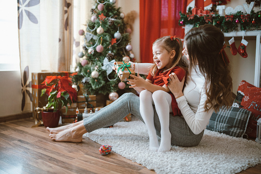 Mother and her little daughter are having fun surrounded by Christmas decoration at Christmas holidays at home and giving each other gifts