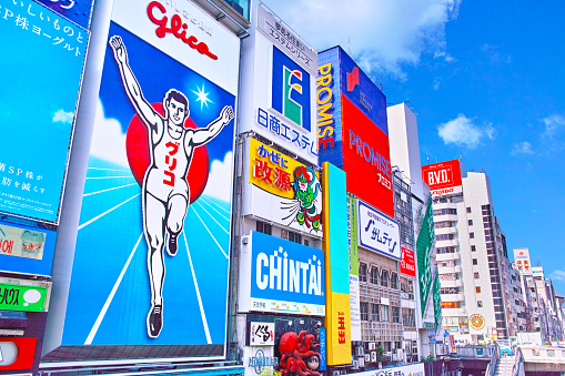 Scenery with signs of tourist spots along the Dotonbori River in Namba, Osaka at noon.