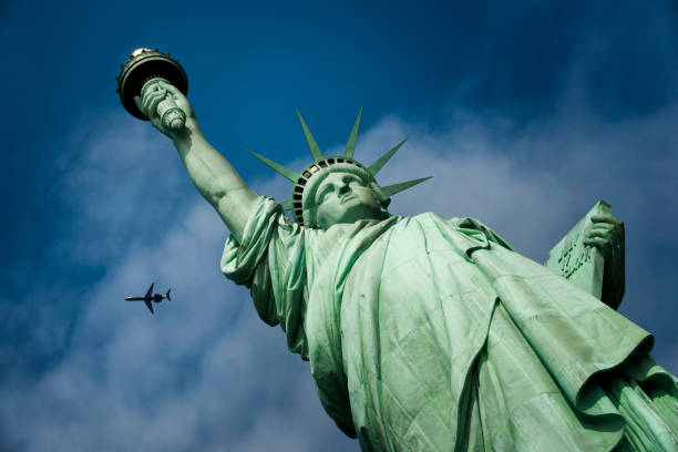 un avion survole la statue de la liberté à new york - statue of liberty liberty statue flaming torch photos et images de collection