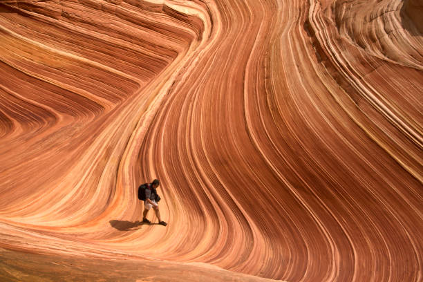 Hiking at The Wave in Arizona Man walks through distinctive striated rock patterns at The Wave; Coyote Butte;  Paria Canyon Vermillion Cliffs Wilderness, Kanab, AZ; USA the wave arizona stock pictures, royalty-free photos & images