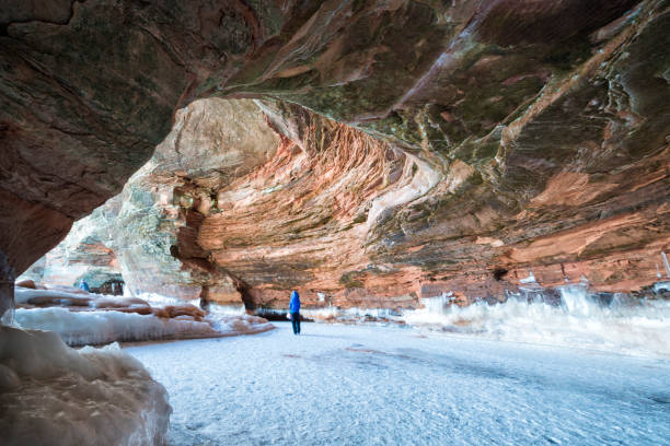 Woman walking through sandstone cavern visiting the ice caves at Apostle Island National Lakeshore, Cornucopia, Bayfield County, Wisconsin, USA