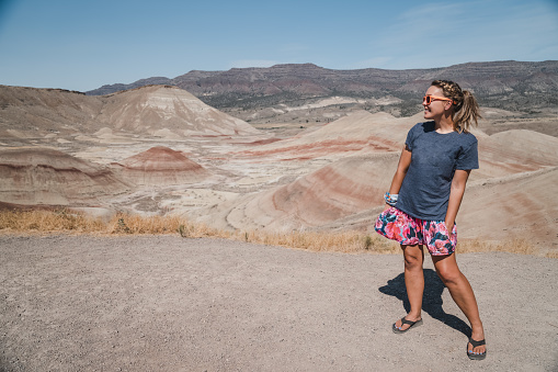 Cute playful woman in casual clothing poses with hands in pockets at the Painted Hills overlook at the John Day Fossil Beds National Monument