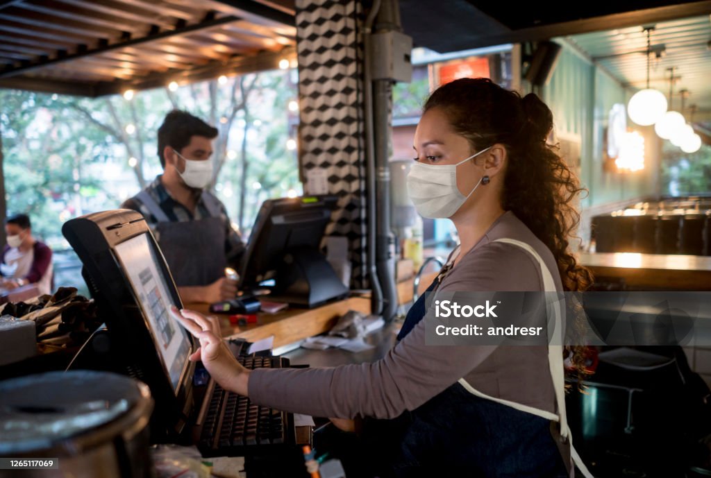 Woman working at the cashier at a restaurant wearing a facemask Portrait of a woman working at the cashier at a restaurant wearing a facemask - food service occupation concepts Protective Face Mask Stock Photo