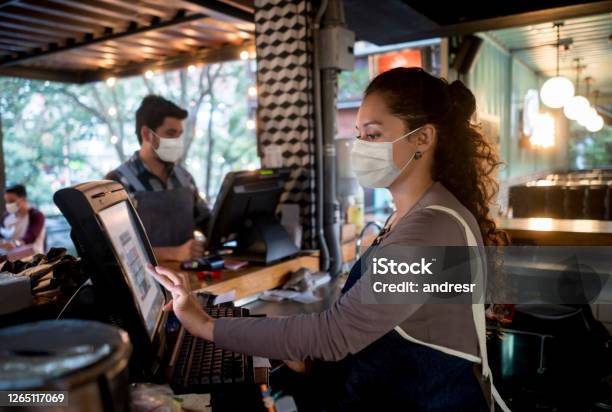 Woman Working At The Cashier At A Restaurant Wearing A Facemask Stock Photo - Download Image Now