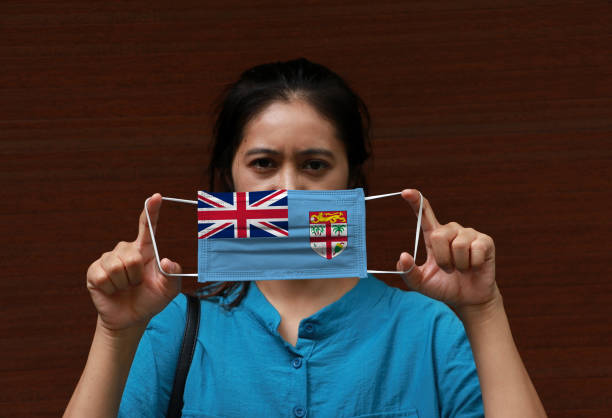 una mujer con bandera de fiji en máscara higiénica en la mano y levantó la cara frontal sobre fondo marrón. - arms lifted fotografías e imágenes de stock