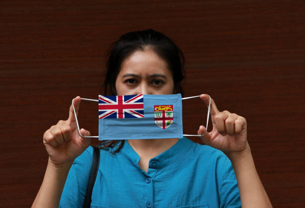 A woman with Fiji flag on hygienic mask in her hand and lifted up the front face on brown background. stock photo