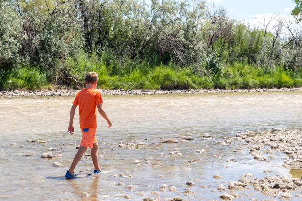 tween boy guadare in un fiume fangoso poco profondo - wading child water sport clothing foto e immagini stock