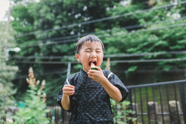 Japanese boy wearing yukata, summer kimono, and eating watermelon in summer.