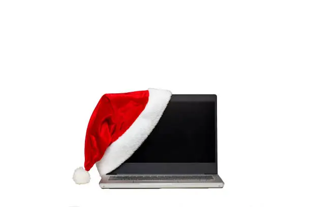 Laptop on a white isolated background. A hat of santaclaus lies on a laptop. The end of the working year. Holiday sales.