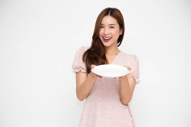 istock Young Asian woman holding empty white plate or dish isolated on white background 1265145838