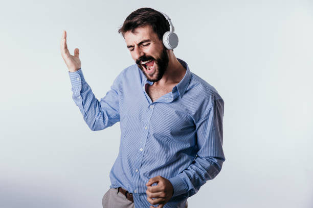 Casual Business Studio Attractive happy bearded male standing isolated in a blue shirt, singing, and playing air guitar with headphones on. air guitar stock pictures, royalty-free photos & images