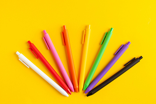 Multi-colored pens on a yellow background. The concept of the beginning of the school year, office supplies, school supplies. High quality photo