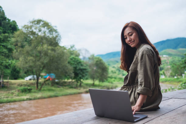 istock a beautiful asian woman working on laptop computer while sitting by the river with mountains and nature background 1265154702