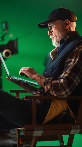 istock Prominent Successful Director Sitting in a Chair on a Break and Using Laptop Computer. On the Studio Film Set with High-End Equipment Professional Crew Shooting High Budget Movie 1265157327