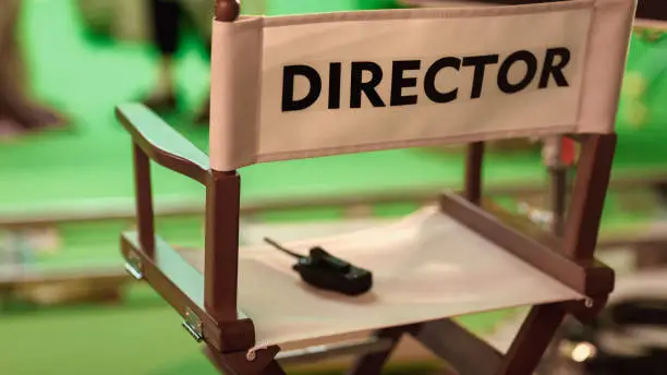 Photo of On Film Studio Set Close Up Shot of Empty Director's Chair. In the Background Professional Crew Shooting Green Screen Scene with Actors for History Movie.